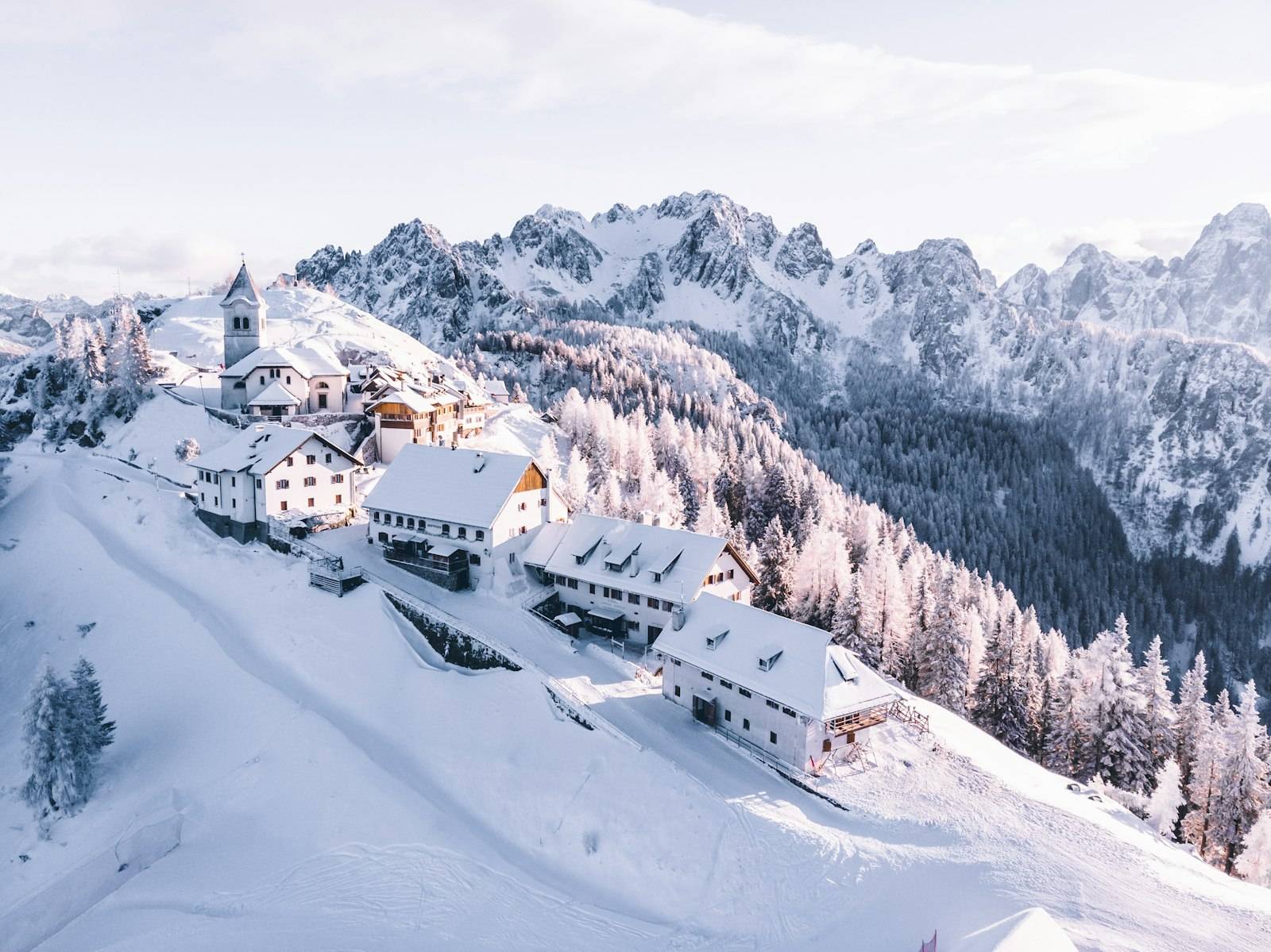 A snow-covered alpine village with a church on the ridge above frosted pine forest