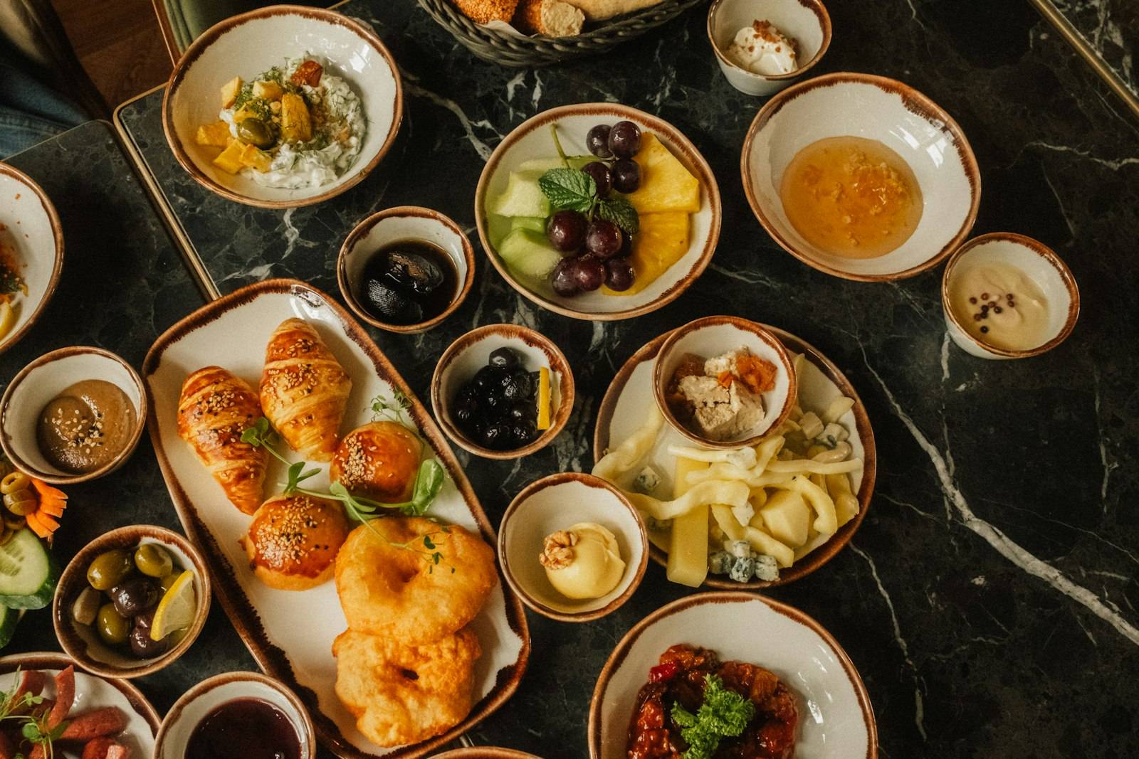 A generous French breakfast spread with croissants, pastries, fruit, yoghurt, olives and cold cuts laid out on a table