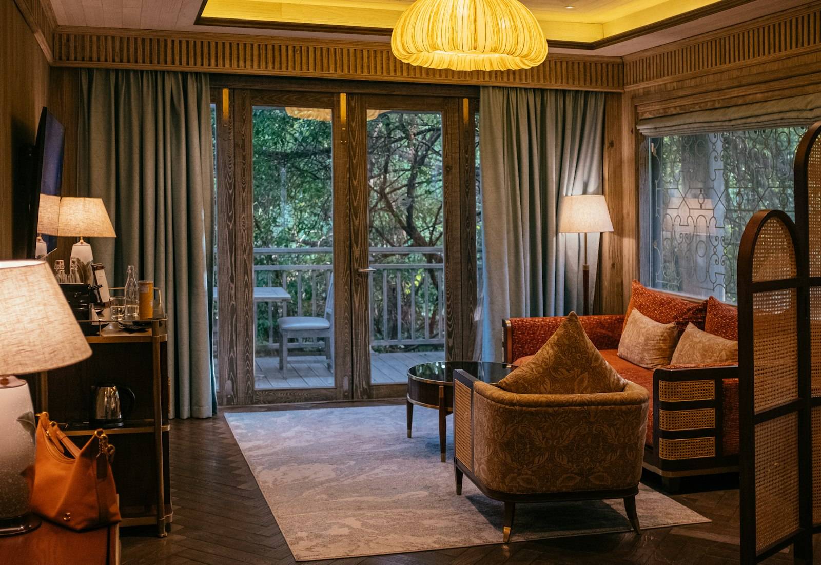 A luxury hotel suite with warm wood panelling and a balcony terrace overlooking trees